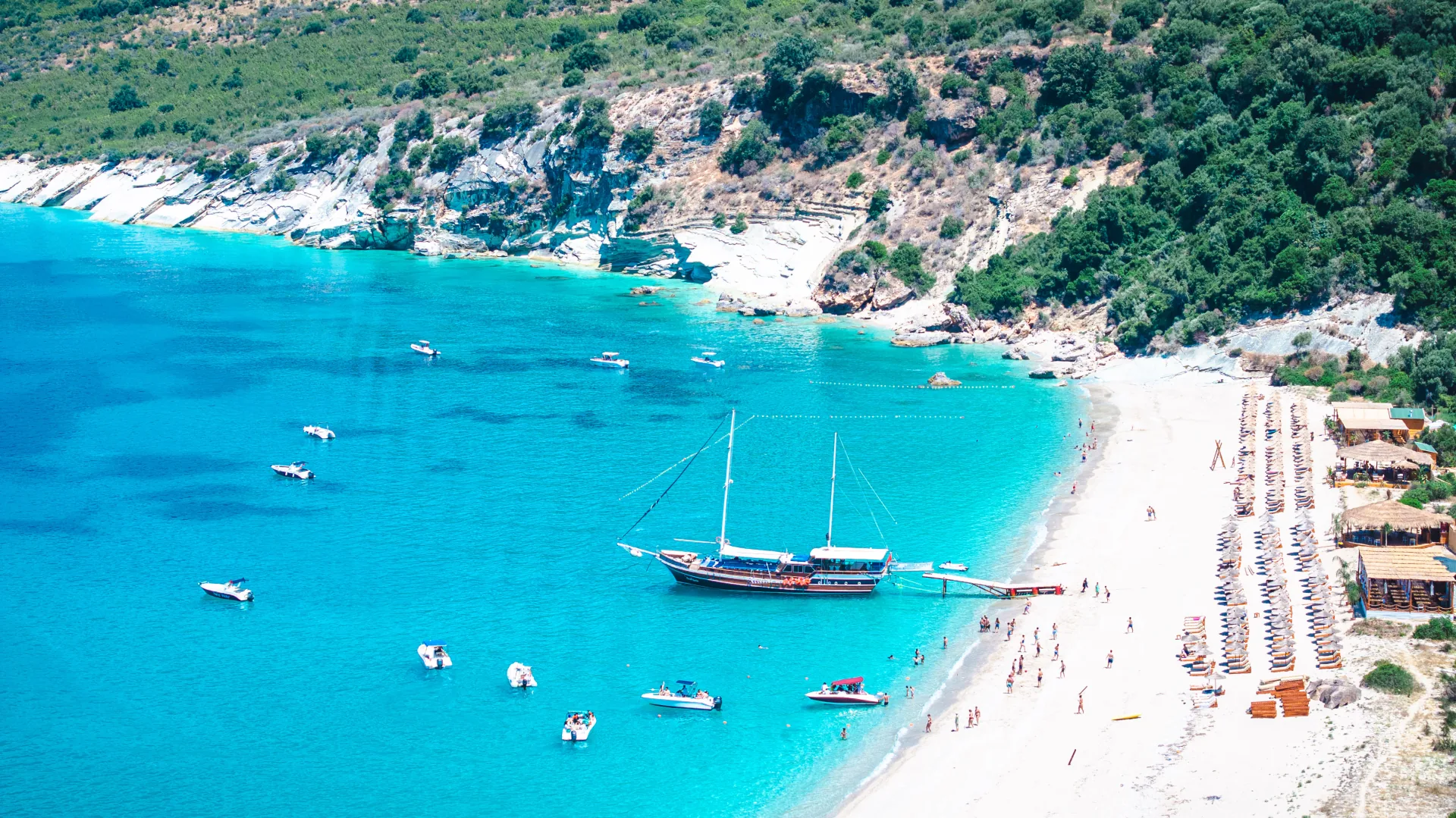 Aerial drone view of a long Albanian Riviera beach with a traditional gulet anchored offshore
