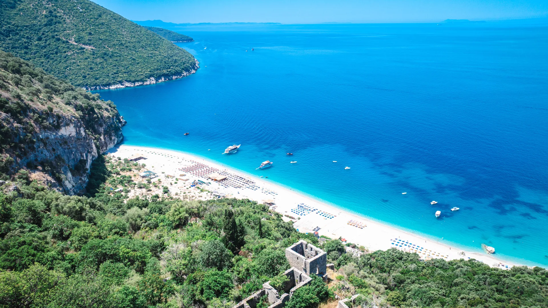 Aerial drone view of a hidden Albanian Riviera beach with an old stone tower and turquoise water
