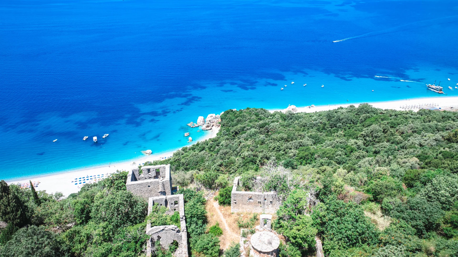 Aerial of an old stone watchtower above a turquoise Albanian Riviera bay
