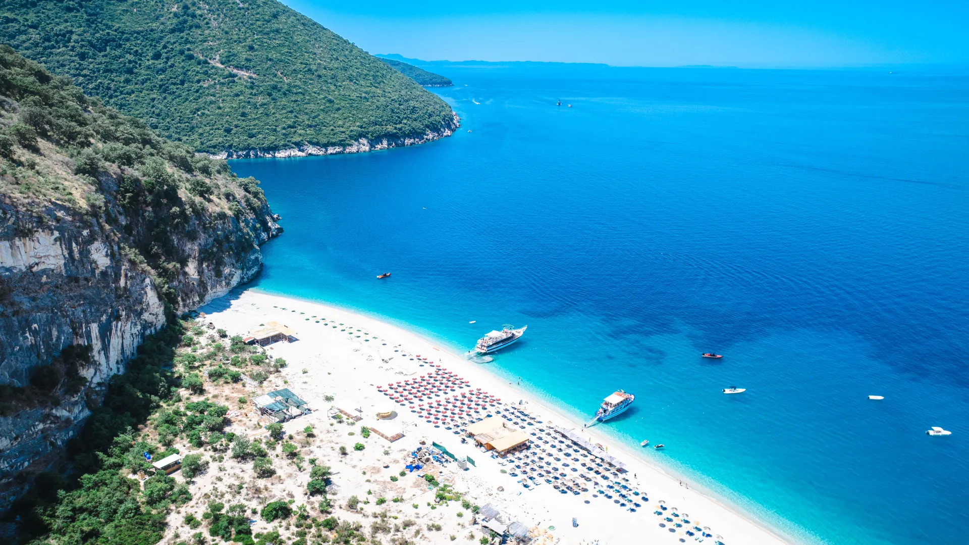 Aerial drone view of a long sandy beach near Saranda with rows of umbrellas and turquoise water