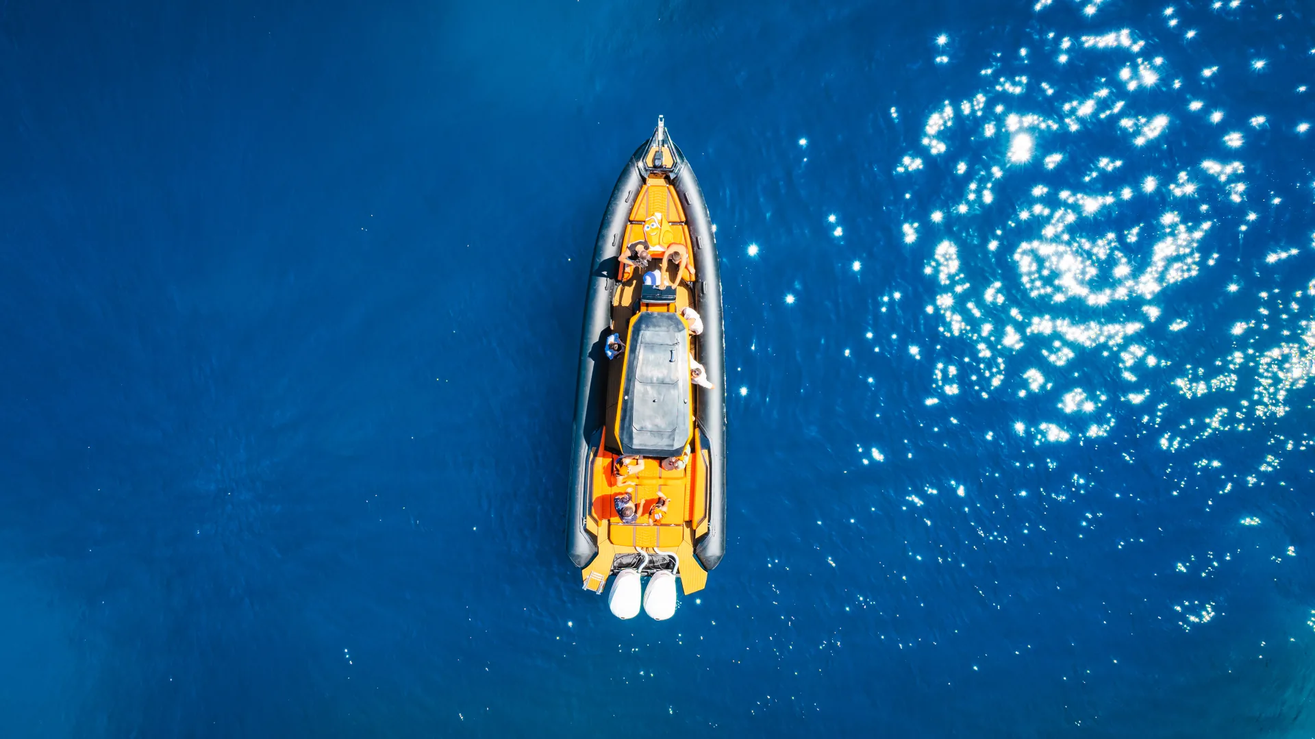 Top-down aerial of the Nemo Boat in deep blue water with the sun reflecting in stars across the surface