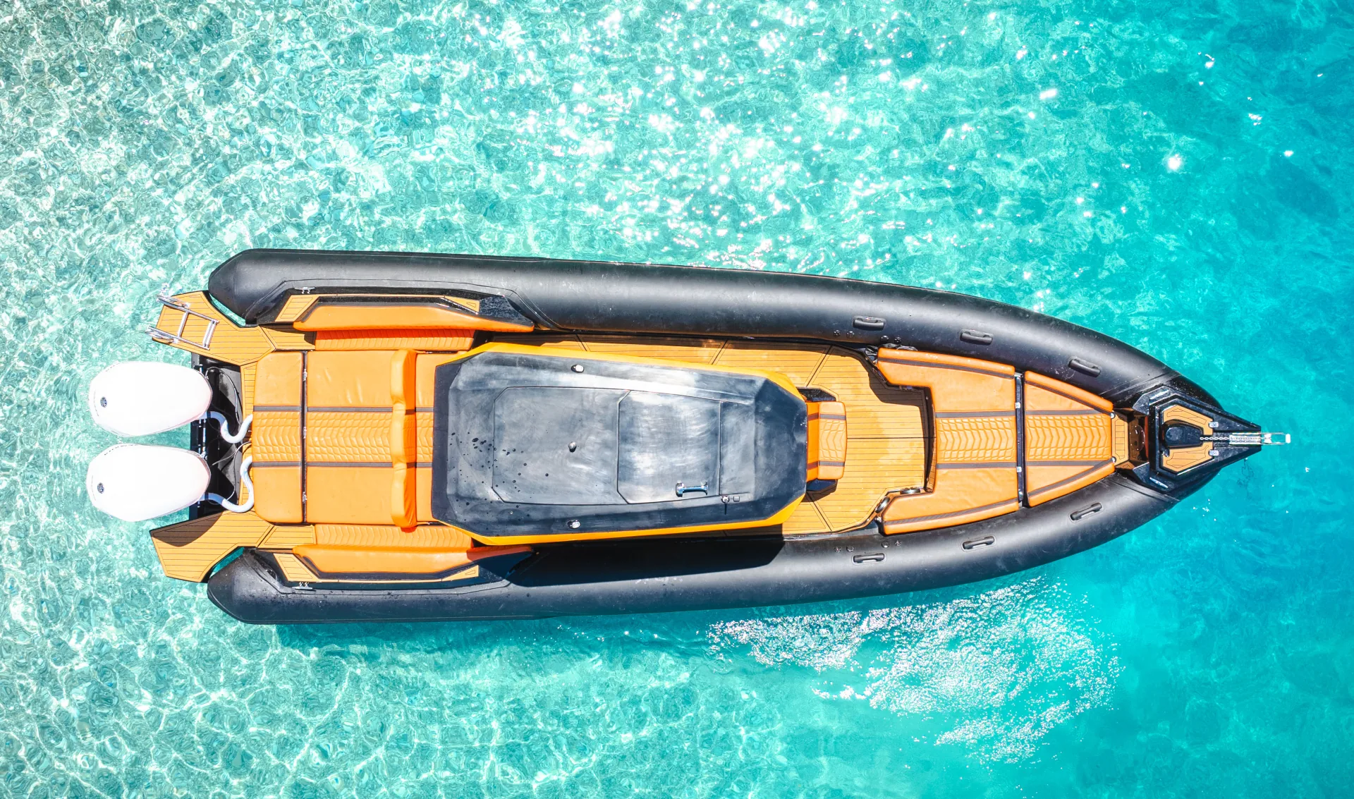 Top-down drone view of a black-and-orange Nemo Boat alone in shallow turquoise water near Ksamil