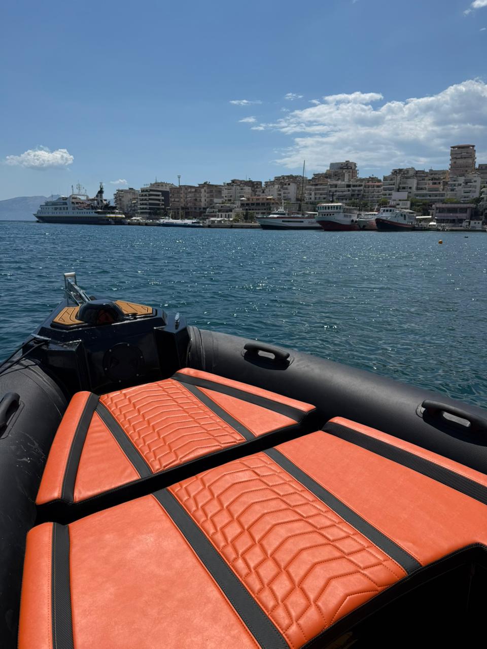 Nemo Boat bow with the helm console and orange quilted seating, Saranda port in the distance