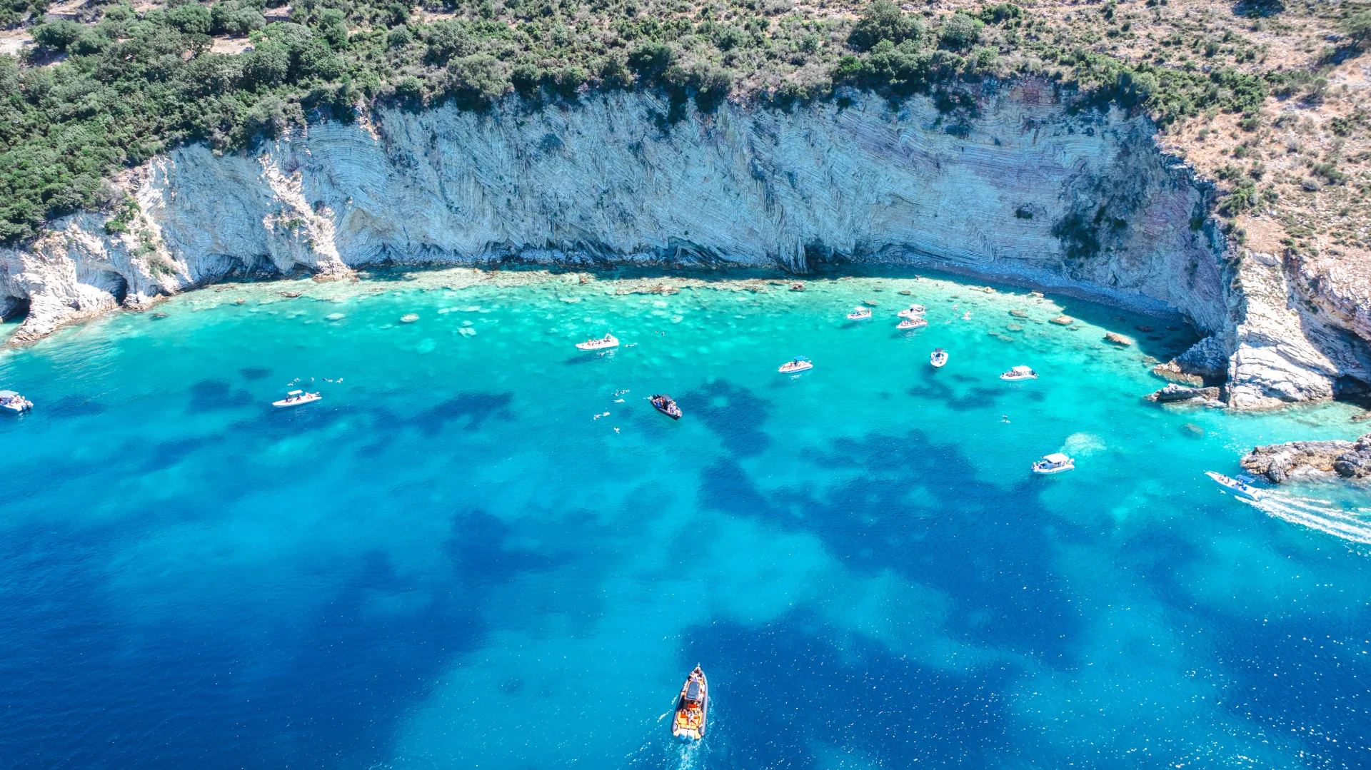 Aerial drone view of multiple boats anchored in a shallow turquoise cove on the Albanian Riviera