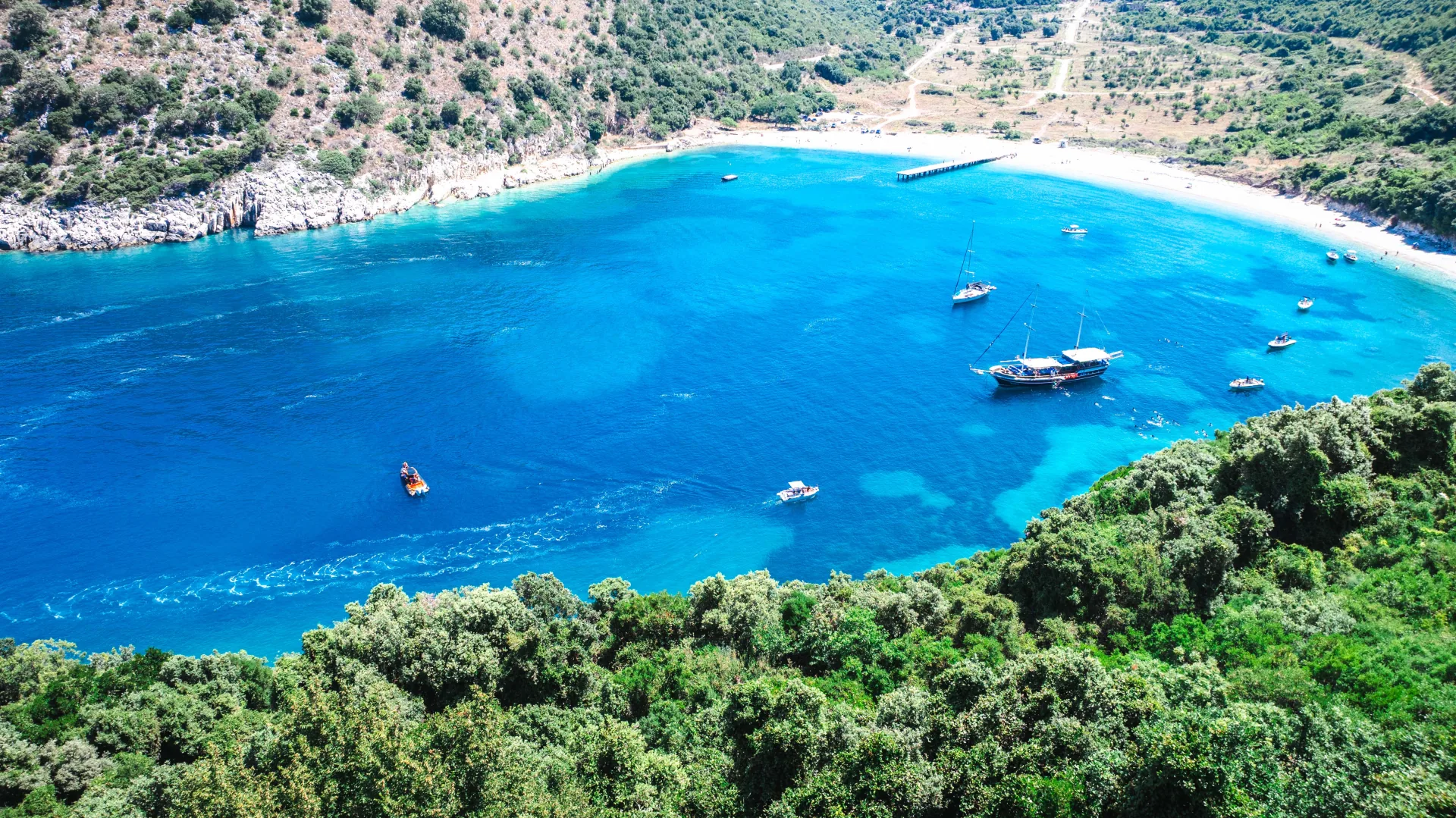 Aerial drone view of a hidden Albanian Riviera cove with a traditional sailing boat and white sand beach